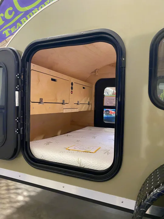 View inside a compact teardrop RV rental: a cozy mattress and wooden storage are visible through the open side door.. TC Tear Drop TC Original 2022