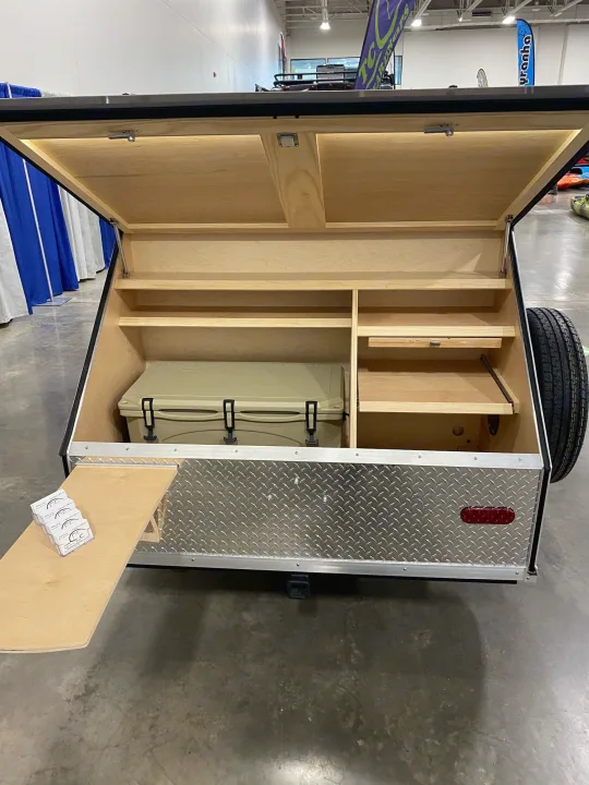 Inside a compact camping trailer, an RV rental add-on, showing cooler space, shelves, and a pull-out counter for outdoor gear.. TC Tear Drop TC Original 2022