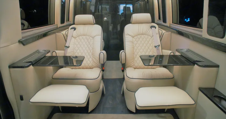 Comfortable RV rental interior: two plush cream captain's chairs, each with a glossy table, cup holder, and footrest.. Ultimate Toys Ultimate Coach 2022