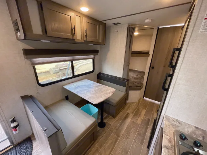 RV rental interior: Dinette, overhead cabinets, bunk beds, kitchen, and wood-look flooring are visible in this camper.. Gulf Stream Kingsport 2021