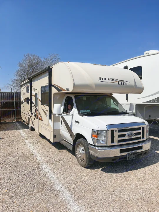 Freedom Elite RV rental parked on gravel, with a smiling child in the window. Perfect for your next adventure!. Thor Freedom Elite 2017
