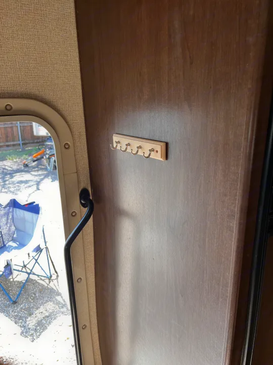 Inside an RV rental: A door features a wooden key holder with four metal hooks. A window shows outdoor chairs and a yard.. Thor Freedom Elite 2017
