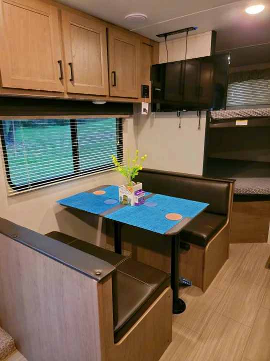 Cozy RV rental interior featuring a dinette with bench seating, TV, and wood-look cabinets. Ideal for travel.. Keystone Hideout 2021
