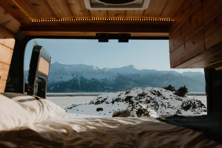 Cozy rv rental with rear door open to a stunning snowy mountain landscape, lake, and rocky foreground from the bed.. Dodge Ram 2500 (Class B) 2021