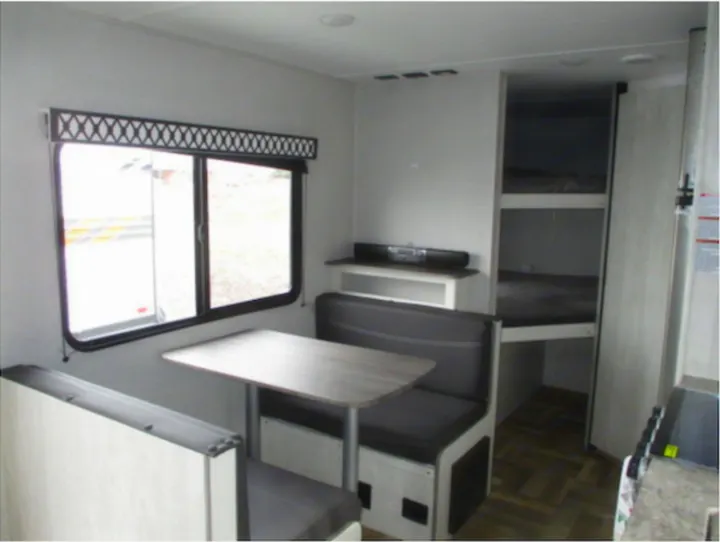 RV rental interior shows a light-colored dinette with gray seats, large window, entertainment shelf, and bunk beds to the right.. Shasta Shasta Travel Trailer 26BH 2022