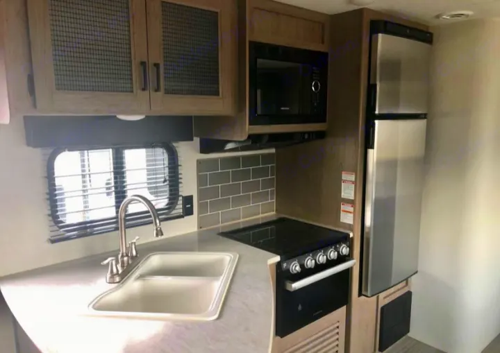 Explore this RV rental's modern kitchen, featuring a sink, stove, microwave, and stainless steel refrigerator.. Keystone RV Hideout LHS 2021