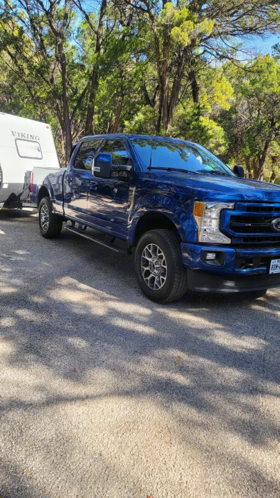 A blue Ford truck tows a white Viking travel trailer (an RV rental) parked on gravel, surrounded by trees.. Coachmen Viking 2019
