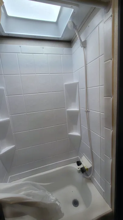 Inside a bright, clean white RV rental shower: handheld shower, controls, drain, skylight, and grid-patterned walls.. Coachmen Viking 2019