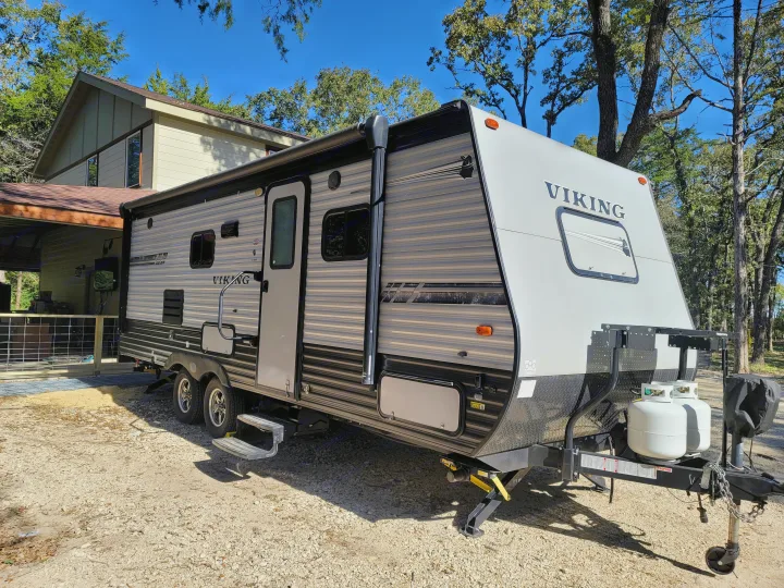A modern Viking travel trailer, ready for your next adventure as an RV rental, is parked beside a house and trees.. Coachmen Viking 2019