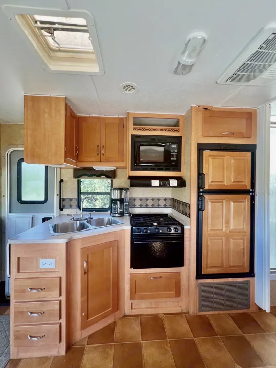 Explore this clean RV rental kitchen, equipped with a sink, stove, microwave, fridge, wood cabinets, and tile floor.. Forest River Sunseeker 2009