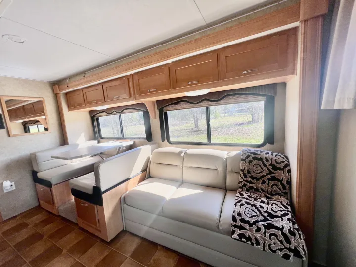 Spacious rv rental interior featuring a dinette, sofa, and overhead storage. Enjoy the view through large windows!. Forest River Sunseeker 2009