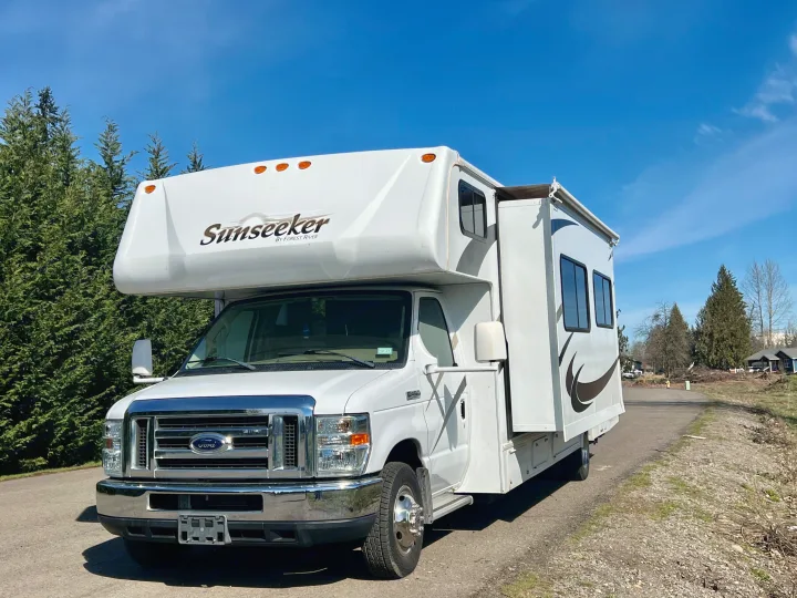 This white Sunseeker Class C rv rental is parked outdoors on a bright, sunny day, with its slide-out extended.. Forest River Sunseeker 2009