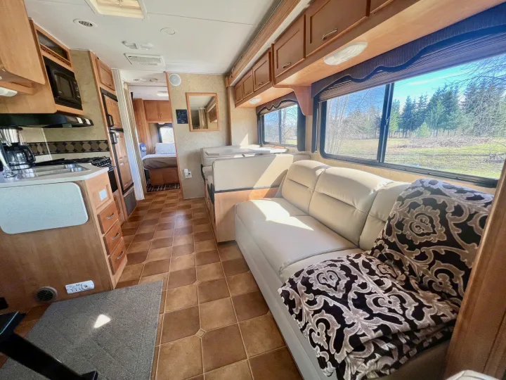 Spacious RV rental interior with bright living area, full kitchen, and comfortable bedroom. Enjoy scenic views from large windows.. Forest River Sunseeker 2009