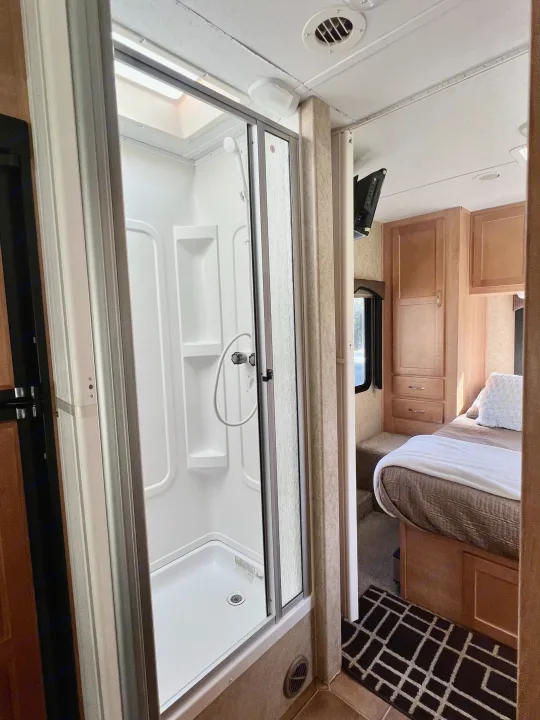Cozy RV rental interior, showcasing a bright stand-up shower stall and a glimpse into a comfortable bedroom with wooden cabinetry.. Forest River Sunseeker 2009
