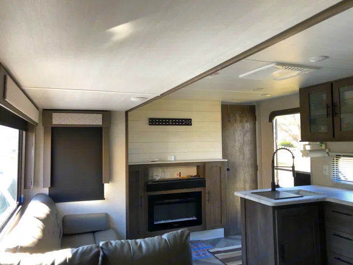 Inside this modern RV rental: a comfortable living area with a sofa, entertainment center, fireplace, and full kitchen.. Forest River Wildwood 2020