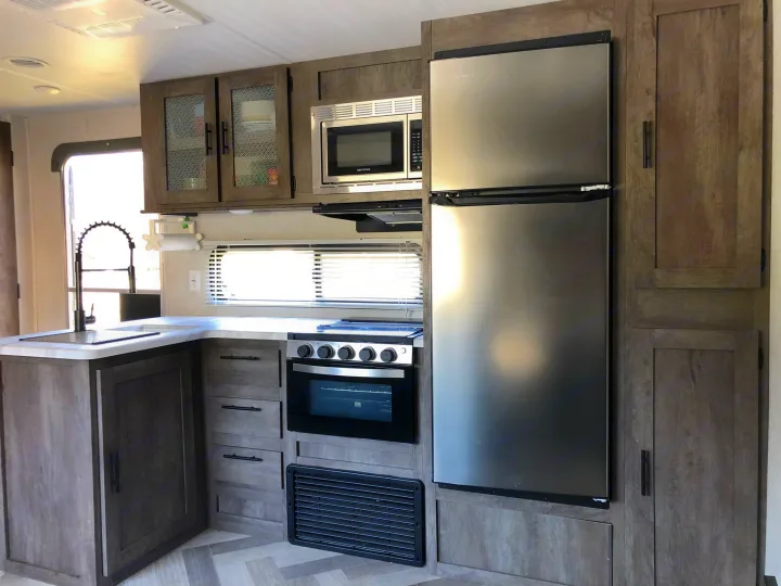 This RV rental features a modern kitchen with stainless steel refrigerator, oven, microwave, and wood-grain cabinetry.. Forest River Wildwood 2020