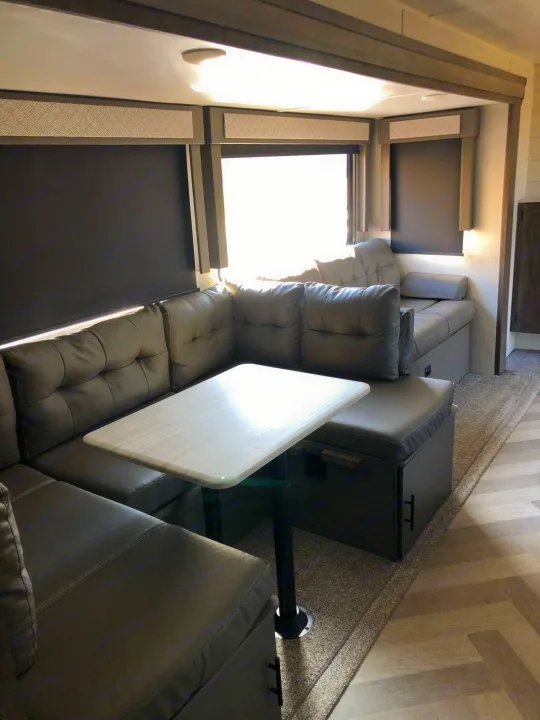 An RV rental features a comfortable dinette with dark gray upholstered seating, a white table, and large windows.. Forest River Wildwood 2020