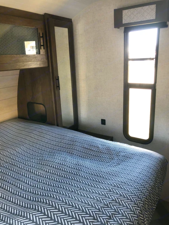 Experience comfort in this modern RV rental bedroom featuring a patterned bed, cabinet storage, window, and USB port.. Forest River Wildwood 2020
