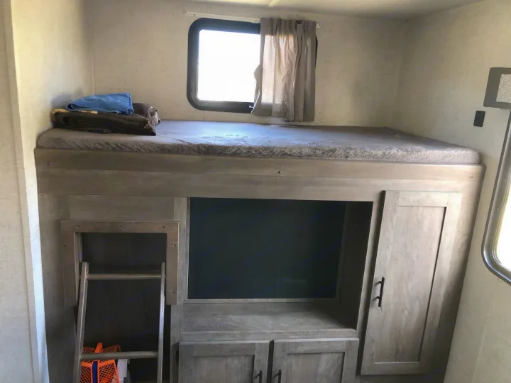 RV rental interior: Bunk bed with window, ladder, and integrated storage/entertainment area below.. Forest River Wildwood 2020