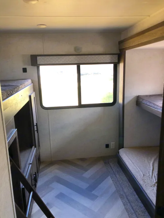 Modern RV rental interior featuring bunk beds, a central window, and stylish flooring, ideal for family trips.. Forest River Wildwood 2020