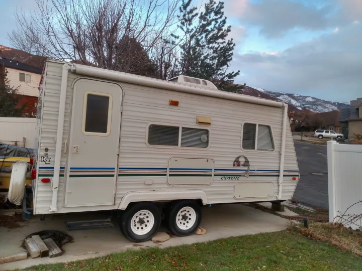 White KZ Coyote travel trailer, ideal for an rv rental, parked in a residential driveway with snowy mountains in the background.. Sportsmen Coyote 2002