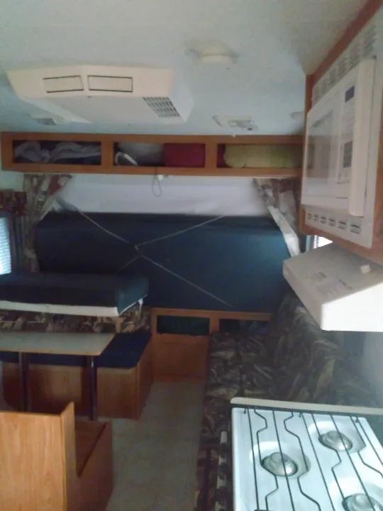 Cozy RV rental interior with dinette, bed, overhead storage, microwave, and stove for your travels.. Sportsmen Coyote 2002