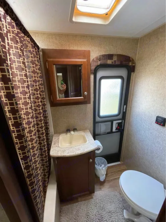This compact RV rental bathroom includes a shower, toilet, sink with vanity, mirror, and an RV entry door.. Sport Trek Sport Trek Trailer 2015