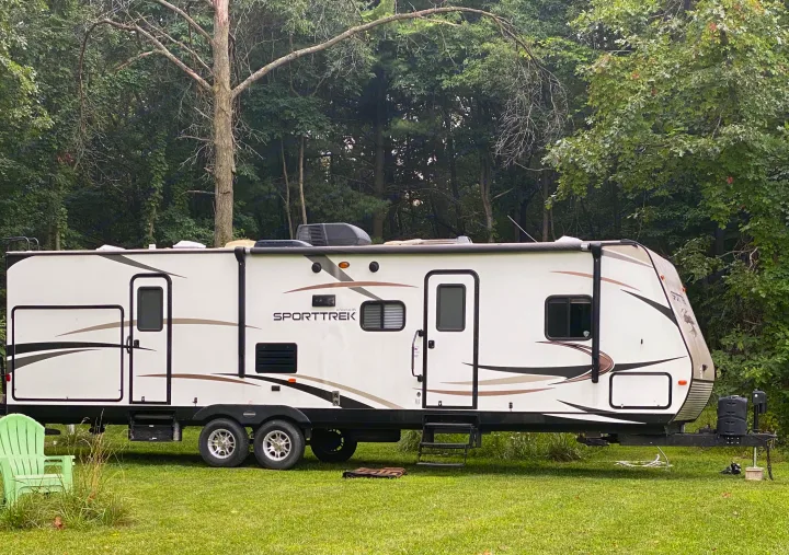 This Sporttrek travel trailer RV rental is parked in a lush, green campsite, surrounded by dense trees.. Sport Trek Sport Trek Trailer 2015