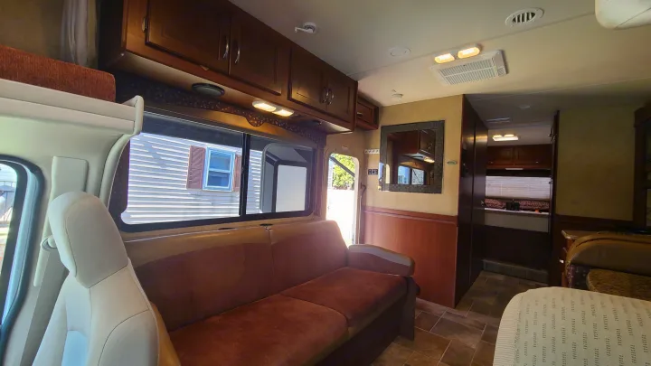 Interior of an RV rental showing a comfortable living area with a sofa, overhead cabinets, and a bunk.. Thor Motor Coach Freedom Elite 2015