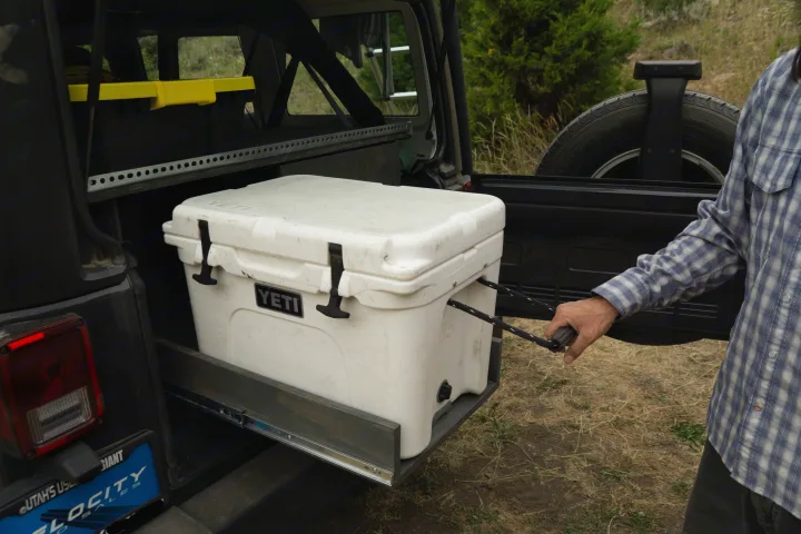 Organized Jeep adventure with an rv rental! Man pulls Yeti cooler from custom slide-out storage system.. Jeep Wrangler Unlimited 2018