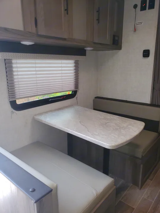 RV rental interior: A bright dinette with a light-colored table, bench seats, and overhead cabinets.. Gulf Stream Amerilite 2021