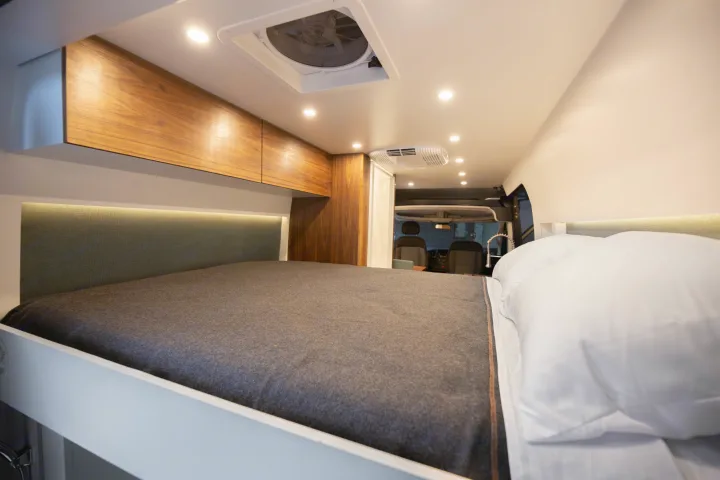 Interior of an RV rental: a modern, comfortable sleeping area with a large bed, sleek wood cabinets & recessed lighting.. Other Other 2021