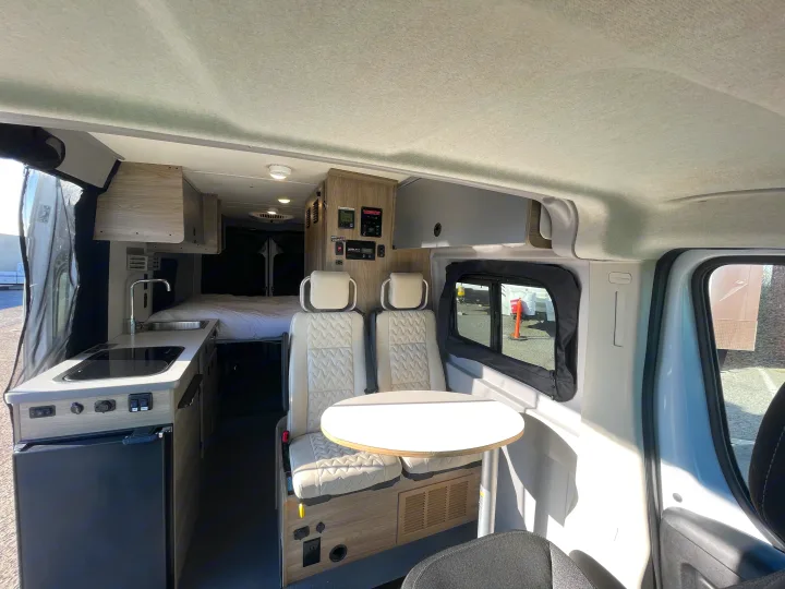 Modern rv rental interior featuring a compact kitchen, comfortable bed, and versatile seating with a table.. Winnebago solis 2022