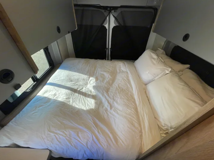 Bright and comfortable RV rental sleeping area with crisp white bedding. Overhead cabinets and rear windows with shades complete this mobile bedroom.. Winnebago solis 2022