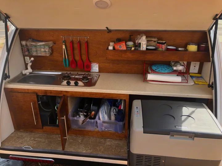This organized RV rental kitchen features a sink, two-burner stove, portable fridge, and clever storage for cooking essentials.. T@B Txl 2018