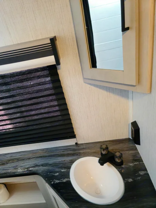 Explore this RV rental's compact bathroom, featuring a white sink, dark counter, window blinds, and mirror.. Heartland mallard 2022