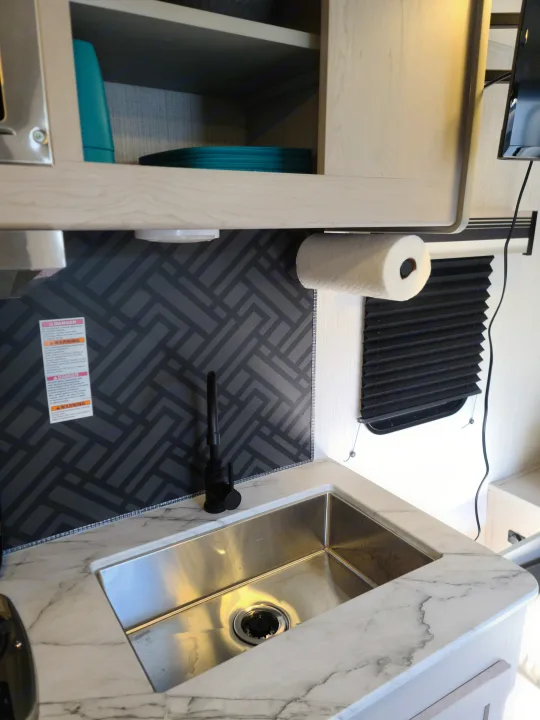 RV rental kitchen featuring a modern sink, sleek black faucet, marble-look counter, and a patterned backsplash.. Heartland mallard 2022