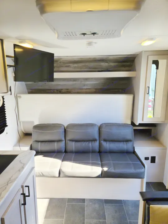RV rental interior shows a black three-seat sofa, mounted TV, kitchen counter, and ceiling AC unit.. Heartland mallard 2022