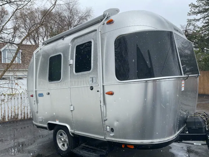 A shiny silver Airstream travel trailer, perfect for an rv rental, glistens with snowflakes while parked outdoors.. Airstream Bambi 2021