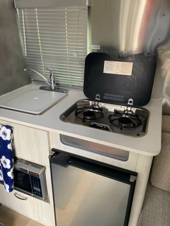 This RV rental kitchenette shows a compact cooking area with a sink, two-burner stovetop, microwave, and refrigerator.. Airstream Bambi 2021