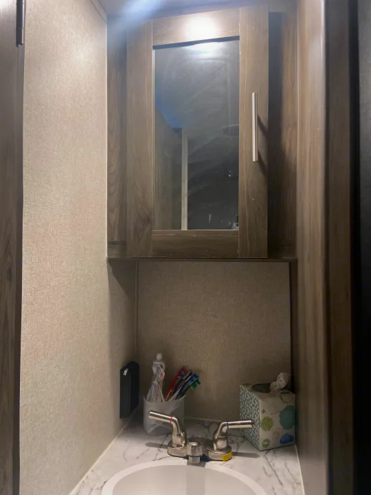 Interior of an RV rental bathroom, showing a sink, faucet, toiletries, and mirrored storage cabinet above.. Clipper Other 2021