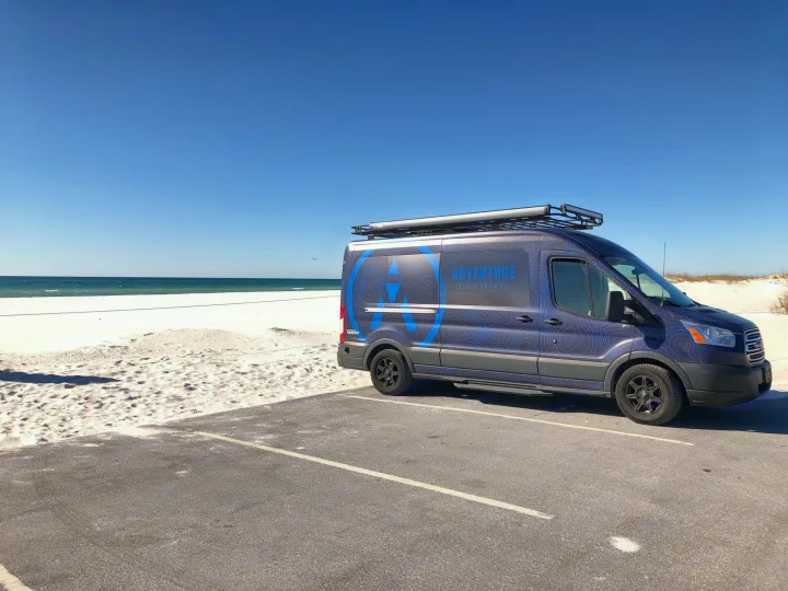 "Adventure Rig Rentals" camper van, an RV rental, by a sunny white sand beach and clear blue ocean.. vandoit DO 2018