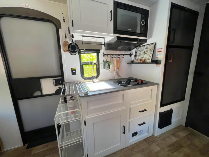 Compact RV rental kitchen with white cabinets, sink, stove, microwave, and exit door.. Keystone RV Hideout 2022