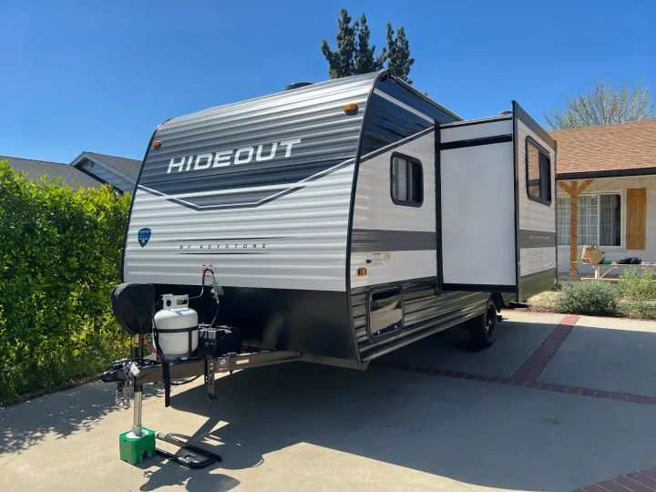 This Hideout by Keystone travel trailer, ideal for an RV rental, sits ready on a driveway with its slide-out extended.. Keystone RV Hideout 2022