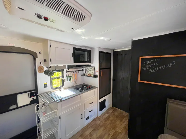 Bright, modern rv rental interior: kitchen with white cabinets, microwave, and fridge, plus exit door. Ready for adventure.. Keystone RV Hideout 2022