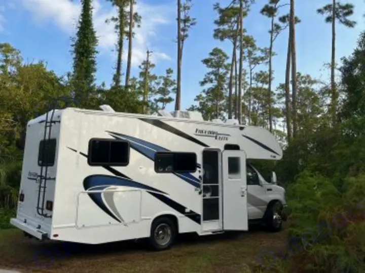 This white Class C RV rental is parked in a peaceful wooded setting with tall pine trees. Perfect for your next outdoor adventure.. Thor Freedom Elite 2021