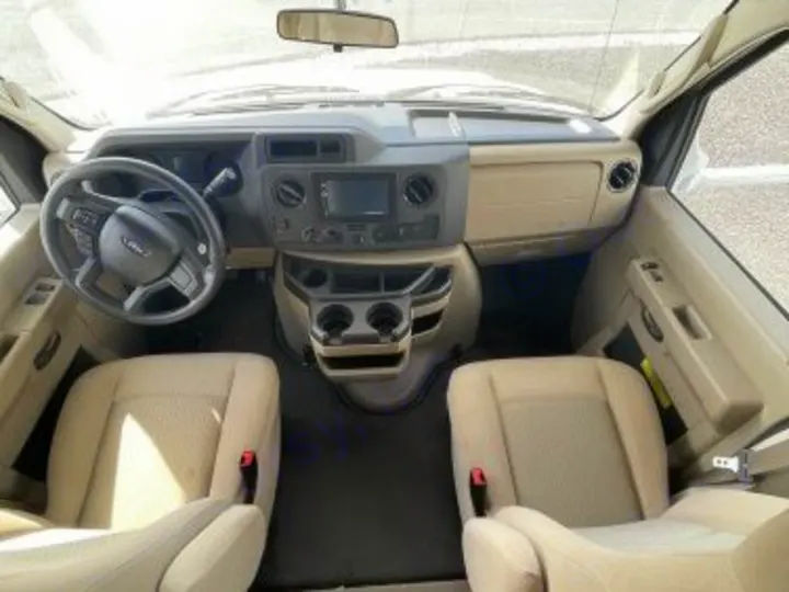 This RV rental's spacious tan interior shows the dashboard, steering wheel, central console with screen/cup holders, and front seats.. Thor Freedom Elite 2021