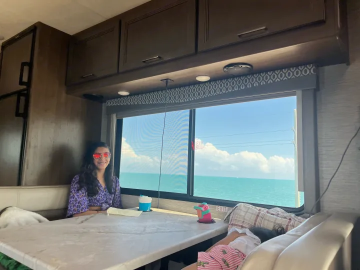 A girl in sunglasses and family relax in their RV rental, enjoying the stunning ocean view from inside.. Thor Freedom Elite 2021