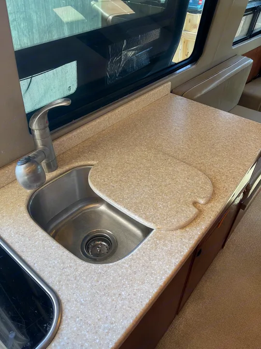 RV rental kitchen: Stainless steel sink, faucet, speckled beige countertop with a cover, and window view in a modern RV.. Sportsmobile Custom Design 2013