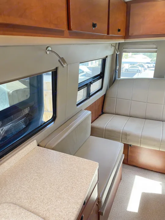 Cozy RV rental interior with light seating, overhead cabinets, and windows showing the outside. Perfect for road trips.. Sportsmobile Custom Design 2013